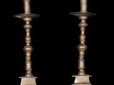 pair of antique brass candlesticks on pedestals against a black background