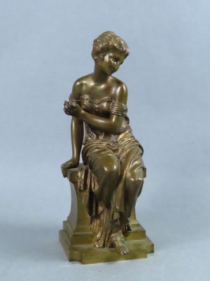 an antique bronze statue of a woman sitting on a rock