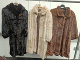 three coats of fur are hanging on a rack in a room