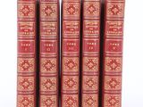 six red books with gold trims are lined up on a white surface