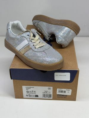 des baskets argentées pailletées avec des lacets blancs, posées sur une boîte en carton