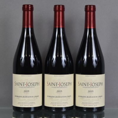trois bouteilles de vin rouge sont posées sur une table en verre