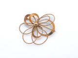 Broche en forme de fleur plaquée or jaune, ornée d'une corde torsadée sur fond blanc