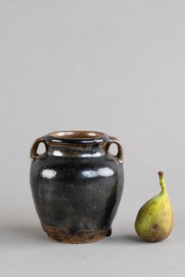 un petit vase noir posé à côté d'une poire sur une table