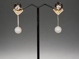 a pair of gold and pearl earrings on a black stand