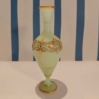 a green vase sitting on a white table with a blue and white striped chair in the background