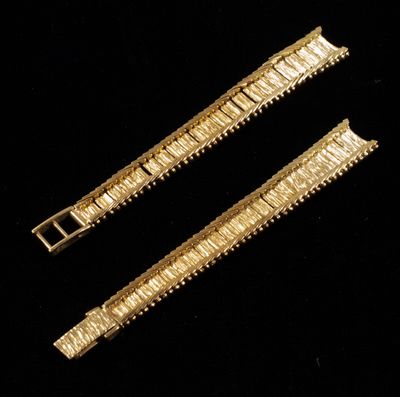 two pieces of gold colored metal bracelets on a black background
