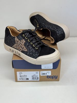des baskets noires à imprimé léopard, avec des lacets, posées sur une boîte en carton
