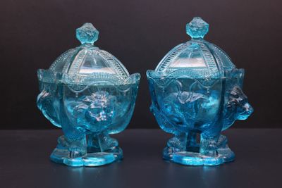 une paire de bonbonnières en verre bleu avec couvercles, posées sur un support noir
