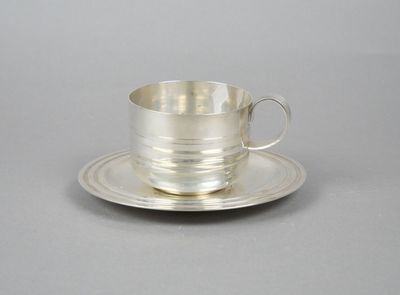 silver cup and saucer with saucer on plate on grey background