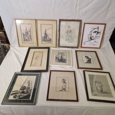 de nombreux tableaux encadrés posés sur une table recouverte d'une nappe blanche
