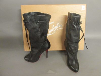 une paire de bottes noires en cuir à talons hauts, avec des lacets, accompagnée d'une boîte