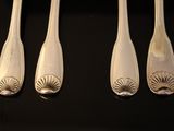 four silver spoons with designs on them sit on a black surface