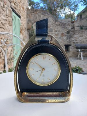 une petite horloge posée sur une table devant un bâtiment en pierre