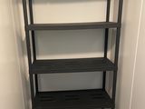 une étagère noire à quatre tablettes, placée dans un coin de la pièce