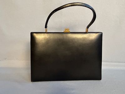 un sac à main noir muni d'une poignée dorée, posé sur une surface blanche