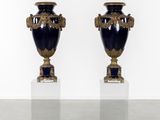 une paire de vases bleus et dorés posés sur des socles, devant un mur blanc