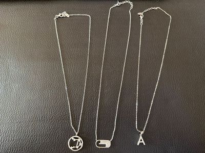 trois colliers en argent ornés de breloques en forme d'initiales, posés sur une table