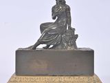 bronze statue of a woman sitting on a rock with a basket of flowers