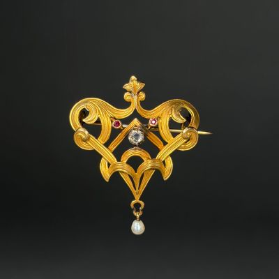 a close up of a gold broochle with a pearl in it