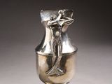a silver vase sitting on a table with a shadow on it