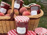 de nombreux pots de confiture posés sur une table, avec un panier de pêches en arrière-plan