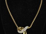 a gold necklace with a diamond bow on a black mannequin
