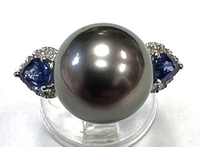 une image d'une bague ornée d'une perle noire et d'un saphir, posée sur un socle transparent