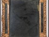 an antique gold framed mirror on a wooden stand with a black background