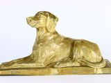 statue dorée représentant un chien, posée sur un socle en bois, sur fond blanc