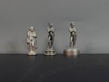 trois figurines en argent représentant un homme et une femme, posées sur des socles