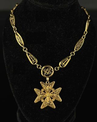a gold plated necklace with a cross pendant on a black mannequin