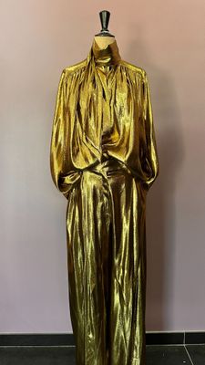une robe dorée métallisée posée sur un mannequin devant un mur rose