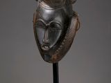 un masque en bronze posé sur un socle noir, avec un fond gris