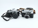 two cameras sitting next to each other on a white surface