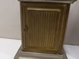 a small brass clock on a stand on a white surface