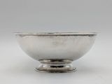 a silver bowl on a stand on a white surface