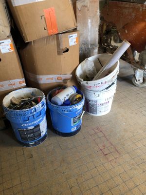 several buckets of paint sitting on the floor next to a pile of boxes