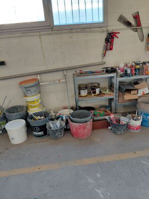 Plusieurs seaux de peinture sont alignés sur le sol d'un garage