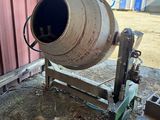 a cement mixer sitting in the dirt outside of a building