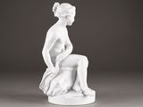 white statue of a woman sitting on a stool with her legs crossed