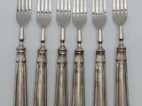 six forks and a knife are lined up on a white surface