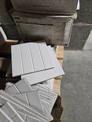 une pile de carreaux blancs posée sur une palette, à côté d'une pile de cartons