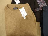 three men ' s sweaters are sitting on a couch with tags on them