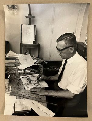 photographie en noir et blanc d'un homme assis à un bureau, entouré de papiers