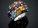 a close up of a ring with multi colored stones on a black surface