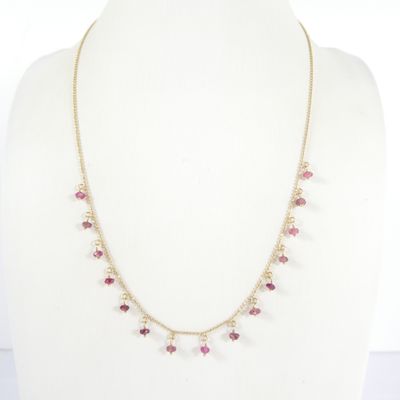a gold necklace with pink stones and pearls on a mannequin