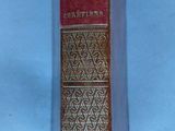 an old book with a red cover sitting on a blue surface