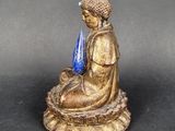 a statue of a person sitting on a rock with a blue vase in his hand