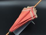 a pink umbrella with lace on it sitting on a stand